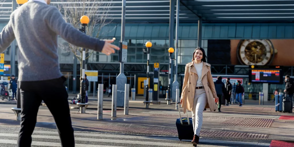 Traveler with luggage warmly greeted by friend outside Heathrow airport terminal in sunshine